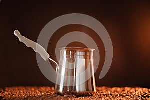 Freshly brewed coffee in cezve on a dark golden background next to scattered roasted coffee beans