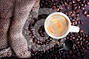 Freshly brewed coffee in a cup on the spilled coffee beans spilling out of the bag