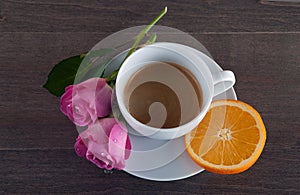 Freshly brewed coffee served with beautiful rose flowers and slice of orange.
