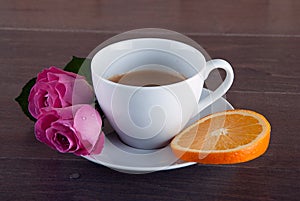 Freshly brewed coffee served with beautiful rose flowers and slice of orange.