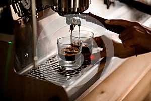 freshly brewed hot espresso is poured from the coffee machine into glass cups
