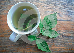 freshly brewed raspberry leaf tea in a white cup and a fresh raspberry leaf