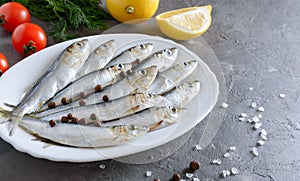 Freshly caught sea small fish on a plate on a gray concrete background with copy space