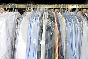 Freshly cleaned men`s shirts and ladies blouses in a dry cleaning, hung on hangers and protected by plastic film.