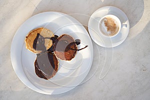Freshly cooked chocolate pancakes poured on a white plate with a cup of fresh coffee. Balanced breakfast. Energy charge. photo