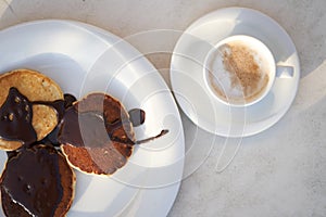 Freshly cooked chocolate pancakes poured on a white plate with a cup of fresh coffee. Balanced breakfast. Energy charge. photo