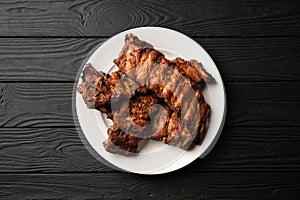 Freshly cooked pork ribs on a white round plate on a black wooden table in the background. Close up, top view.