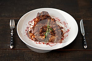 Freshly cooked t-bone steak sprinkled with spices and garnished with a sprig of rosemary on a round white plate with a fork knife