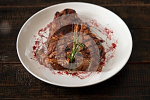 Freshly cooked t-bone steak sprinkled with spices on a round white plate on a wooden dark background. Grilled meat