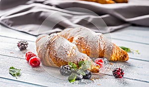 Freshly crispy croissants sprinkled sugar powder with raspberry blackberry and blueberry with mellisa leaves