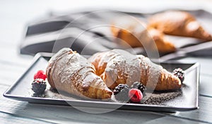 Freshly crispy croissants sprinkled sugar powder with raspberry blackberry and blueberry with mellisa leaves