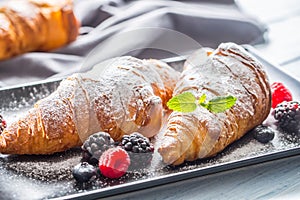 Freshly crispy croissants sprinkled sugar powder with raspberry blackberry and blueberry with mellisa leaves