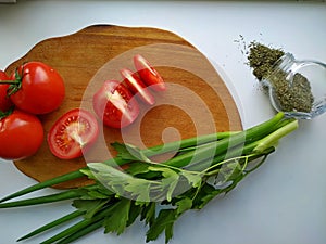 Freshly cut celery, tomatoes, green onion on wooden cutting board next to spiced dill