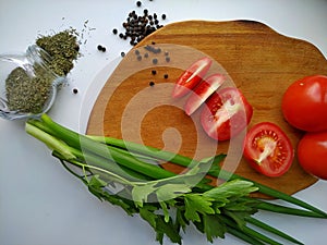 Freshly cut celery, tomatoes, green onion on wooden cutting board next to spiced dill and black pepper