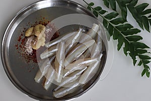 Freshly cut and cleaned anchovy fish presented on a steel plate along with spices for marination photo