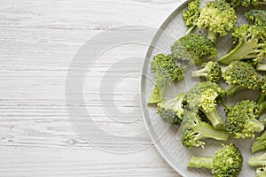 Freshly cut raw broccoli on gray plate over white wooden background, top view. Flat lay, from above, overhead.