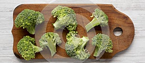 Freshly cut raw broccoli on gray plate on a white wooden table, top view. Flat lay, from above. Close-up