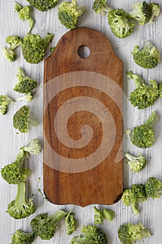 Freshly cut raw broccoli and rustic wooden board on white wooden table, top view. Flat lay, from above, overhead