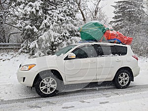 Freshly cut and wrapped Christmas tree on a car roof during heavy snowstorm.