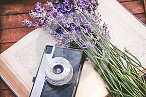 Freshly cutted lavender flowers and a vintage photo camera over an open book.Wooden background.