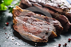 Freshly grilled beef steak on slate plate with salt pepper rosemary and parsley herbs. Sliced pieces of juicy beef steak