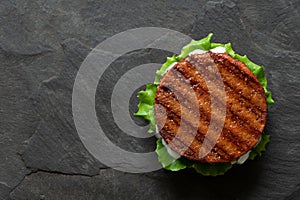 Freshly grilled plant based burger patty on bun with lettuce and sauce isolated on black slate. Top view. Copy space