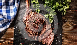 Freshly grilled tomahawk steak on slate plate with salt pepper rosemary and parsley herbs. Sliced pieces of juicy beef steak photo