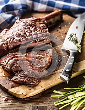 Freshly grilled tomahawk steak on slate plate with salt pepper rosemary and parsley herbs. Sliced pieces of juicy beef steak