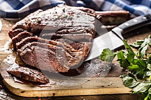 Freshly grilled tomahawk steak on slate plate with salt pepper rosemary and parsley herbs. Sliced pieces of juicy beef steak