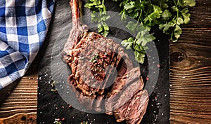 Freshly grilled tomahawk steak on slate plate with salt pepper rosemary and parsley herbs. Sliced pieces of juicy beef steak