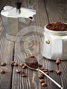 Freshly ground coffee in a spoon, coffee grains are scattered nearby on a brown wooden table. Making fresh aromatic espresso la