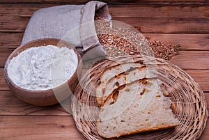 Freshly homemade bread and flour in bowl and wheat grains in bag on wooden table