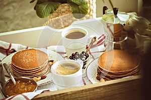 Freshly homemade traditional breakfast for two: pancakes, coffee mugs on tray with checkred cloth