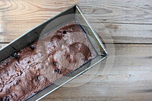 Freshly made brownie chocolate cake with cherries in a baking dish on a wooden table.