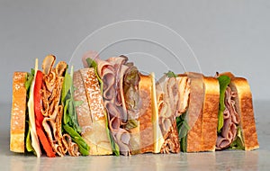 Freshly made deli style sandwich with lettuce, several different kinds of vegetables, tomatoes, cheese, meats similar to ham, photo