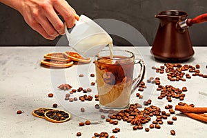 In freshly made espresso coffee in a transparent glass cup, cream is poured from a white cup on a background of gray concrete with