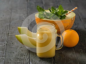 Freshly made melon, orange and banana smoothies and one cocktail tubes on a dark wooden table.