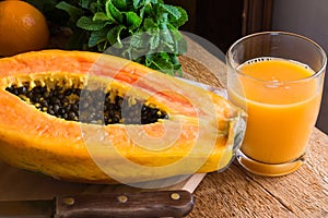 Freshly made papaya juice in glass, fruit cut in half, knife, fresh mint on wood kitchen table