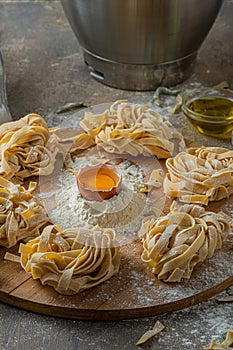 Freshly made tagliatelle pasta with eggs and flour on wooden board