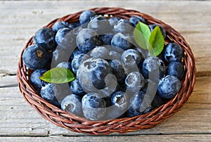 Freshly picked blueberries in a basket on old wooden background.Fresh blueberries with green leaves on rustic table.