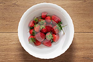 Freshly picked stemmed strawberries in a white bawl set on a wooden table