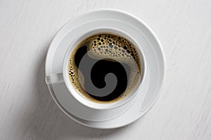 Freshly poured black coffee with froth in white ceramic cup isolated on white from above.