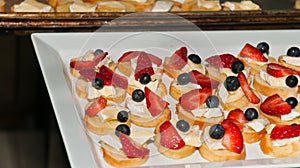 Freshly prepared appitizer of sliced baguette with cheese, blueberry, and halved strawberry