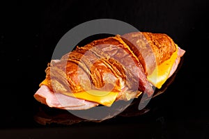 Freshly prepared croissant sandwich, made with ham and cheese, sitting on a black surface