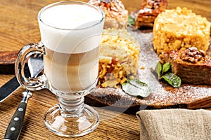 A freshly prepared Cup of frothy lette coffee is served with a piece of cake. On a wooden table