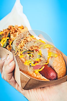 Freshly prepared hotdog with lush salsa in a paper box. Food delivery or junk food concept. Blue background