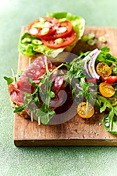 Freshly prepared sandwiches with veggies and salami on wooden chopping board