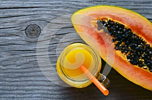 Freshly pressed papaya juice in a glass jar and ripe halved papaya fruit on old wooden table.