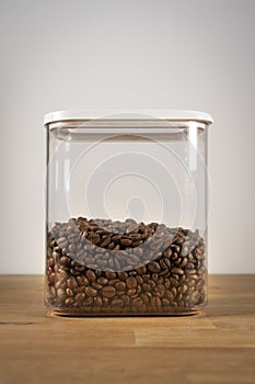 Freshly roasted coffee beans in airtight plastic container on wood table