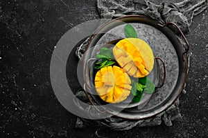 Freshly sliced mango on a metal plate. Tropical fruits. On a black stone background